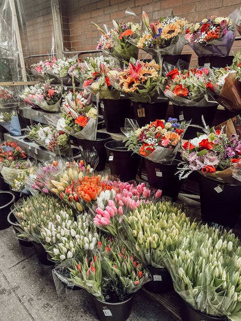 An outdoor display of multiple floral arrangements and bouquets featuring a variety of fresh flowers including tulips, lilies, roses, gerberas, and chrysanthemums in vibrant shades of pink, orange, re