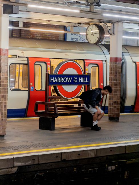 There is no image of flowers or floral arrangements in the provided image. The photo shows a person sitting on a bench at Harrow on the Hill underground station, near a train with the station sign vis
